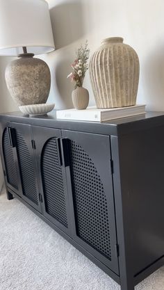 a black sideboard with two vases on top and a lamp next to it