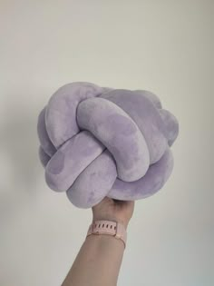 a hand holding up a purple pillow with a knot on it's back and the top