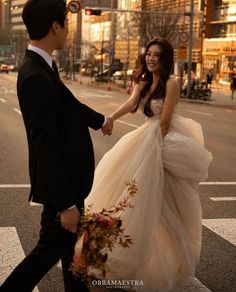 a man and woman are walking across the street holding hands while dressed in formal wear