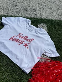 Show your team spirit with our White Cropped T-Shirt, featuring a trendy graphic that says “Football Honey” in bold red lettering. This chic, elegant, boujee, and trendy preppy design is perfect for making a statement on college or professional game days and at tailgate parties. The cropped fit adds a modern, stylish edge, ensuring you stay comfortable and fashionable while cheering on your favorite team. **Key features:**- Chic, elegant, boujee, trendy preppy design- “Football Honey” graphic in bold red lettering- Stylish cropped fit- Soft, comfortable white fabric- Perfect for college and professional game days, and tailgate parties **Keywords:** White Cropped T-Shirt, Football Honey T-Shirt, Trendy Game Day Fashion, Chic Preppy Shirt, Elegant Boujee Style, College Game Day Apparel, Prof Varsity Tops With Team Name For College Events, Cheerleading T-shirt For Football Season With Letter Print, Red Sports Fan T-shirt For Cheerleading, Red Team Spirit T-shirt For Cheerleading, Red T-shirt With Letter Print For Cheerleading, Red T-shirt For Cheerleading With School Spirit, Red T-shirt With Team Name For Cheerleading, Red Cotton T-shirt For Cheerleading, Red Letter Print T-shirt For Cheerleading