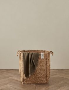 an empty basket on the floor in front of a white wall with a brown scarf hanging from it