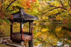 a gazebo sitting in the middle of a lake surrounded by trees with fall colors