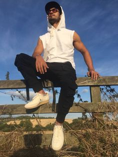 a man sitting on top of a wooden bench wearing a white shirt and black pants