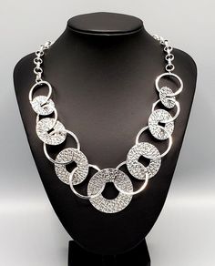 "Industrial Envy": Gradually increasing in size near the center, a collection of shiny silver rings and abstract hammered discs interlock below the collar for an intense industrial look. Features an adjustable clasp closure. Sold as one individual necklace. Includes one pair of matching earrings. Modern Metallic Metal Jewelry, Modern Adjustable Metallic Jewelry, Hammered Silver Jewelry For Party, Modern Circular Metal Jewelry, Metallic Metal Chain Jewelry, Modern Hammered Metal Necklace, Silver Necklace With Unique Round Design, Silver Necklace With Unique Design, Hammered Metal Circle Jewelry