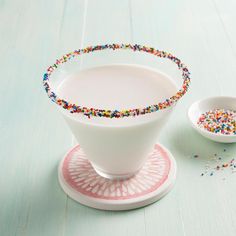 a white bowl filled with sprinkles on top of a wooden table next to a plate