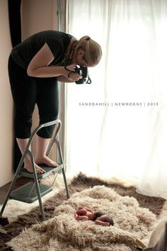 a woman standing on a ladder in front of a window next to a chair and rug