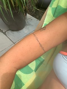 a woman with a small tattoo on her arm sitting next to a potted plant