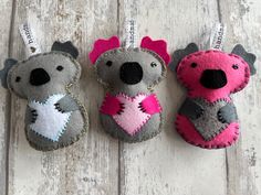 three felt koalas with pink hearts hanging from hooks on a white wooden surface