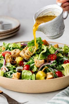 someone pouring dressing onto a salad in a bowl