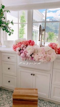 a kitchen with white cabinets and pink flowers on the window sill in front of it