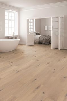 a white bathroom with wood floors and a bathtub in the corner next to a bed