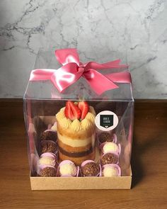 a cake in a box with strawberries on top and cupcakes around it