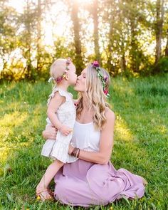 a mother and her daughter are sitting in the grass with their heads touching each other