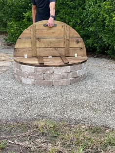 a man standing next to a large wooden barrel on top of a gravel field with trees in the background