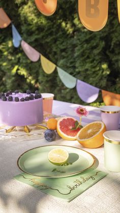 a table topped with plates and cups filled with fruit next to bunting flags that read b