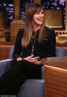 a woman sitting on top of a blue chair in front of a tv screen and smiling