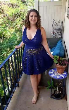 a woman in a blue dress standing on a porch next to a potted plant