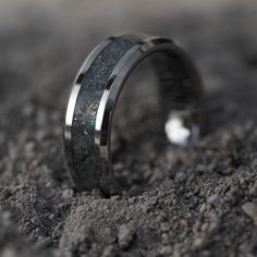 a wedding band with black and white diamonds in it on top of some dirt,