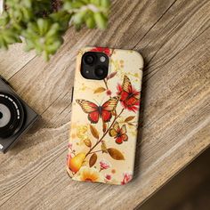 a phone case sitting on top of a wooden table next to a camera and plant