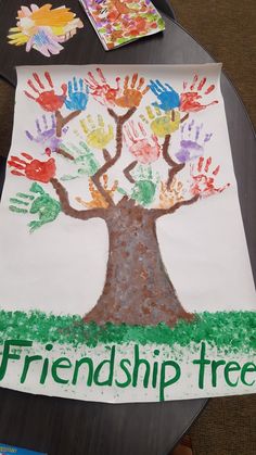 a child's handprinted tree on a table with two children's hands