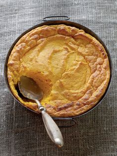 a pie in a pan with a spoon on the side and a cloth tablecloth behind it