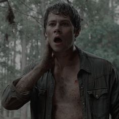 a shirtless man in the woods holding his hand up to his ear and looking surprised