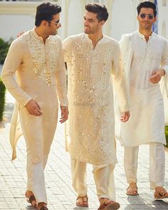 three men in white outfits standing next to each other on a brick floored walkway