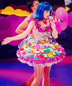 a woman in a dress made out of cupcakes is on stage with microphone