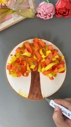 someone is painting a tree on a paper plate with orange and yellow streamers around it