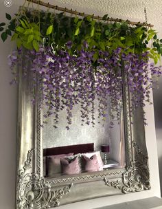 a mirror with purple flowers hanging from it's sides and a bed in the background