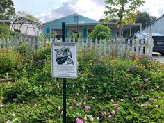 a sign in the middle of a garden with pink flowers and green plants around it