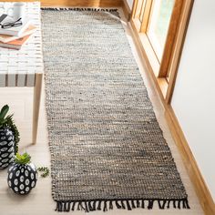 a rug with tassels on the floor next to two vases and a potted plant