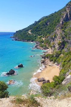 the beach is surrounded by rocky cliffs and blue water, with people walking on it