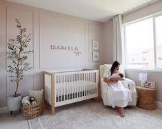 a woman sitting in a chair next to a baby crib with a tree on the wall