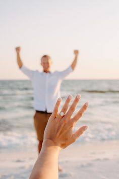 a man standing on top of a beach next to the ocean holding his hands up