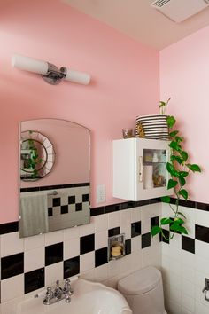 a bathroom with pink walls and black and white tiles on the wall, mirror above the sink