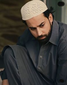 a man sitting on the ground wearing a black shirt and a white headdress