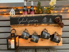 a wooden sign with coffee mugs hanging from it's sides next to candles