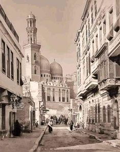 an old black and white photo of people walking down a street with buildings in the background