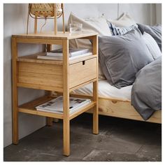 a bed with a wooden night stand on top of it next to pillows and blankets