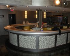 an empty bar in a restaurant with lights on the ceiling and tiled flooring around it