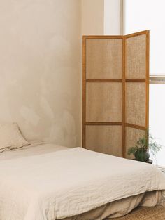 a white bed sitting next to a window with a plant on it's side