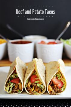 three beef and potato tacos on a white plate with bowls of salsa in the background