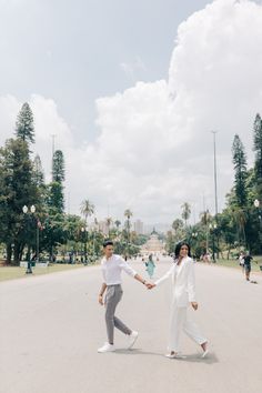 two people are holding hands while walking down the street in front of some palm trees