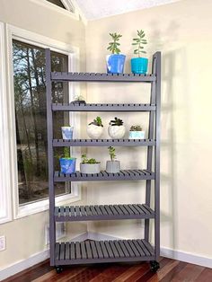 a metal shelf with plants on it in front of a window and wood flooring