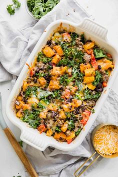 a casserole dish filled with black beans, cheese and vegetables next to a spoon