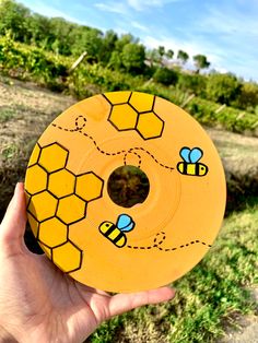 a person holding up a yellow disk with bees on it in front of some trees