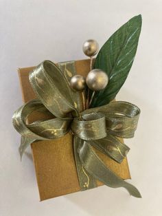 a gift wrapped in gold paper with green leaves and silver balls tied to the top