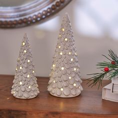 three white ceramic christmas trees on a wooden table with a mirror in the back ground