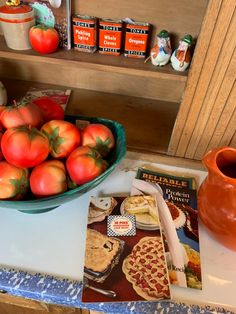 a bowl of tomatoes sitting on top of a counter next to a book and cup